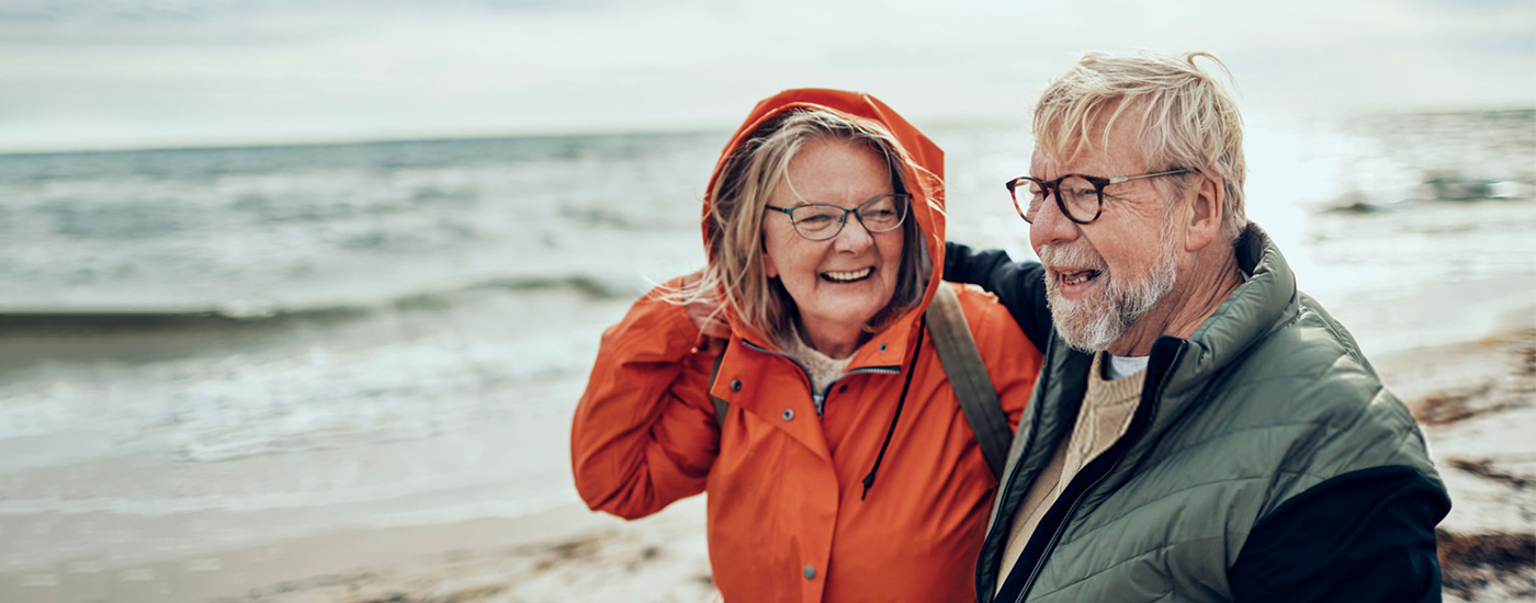 Een ouder echtpaar lacht en glimlacht samen op het strand.